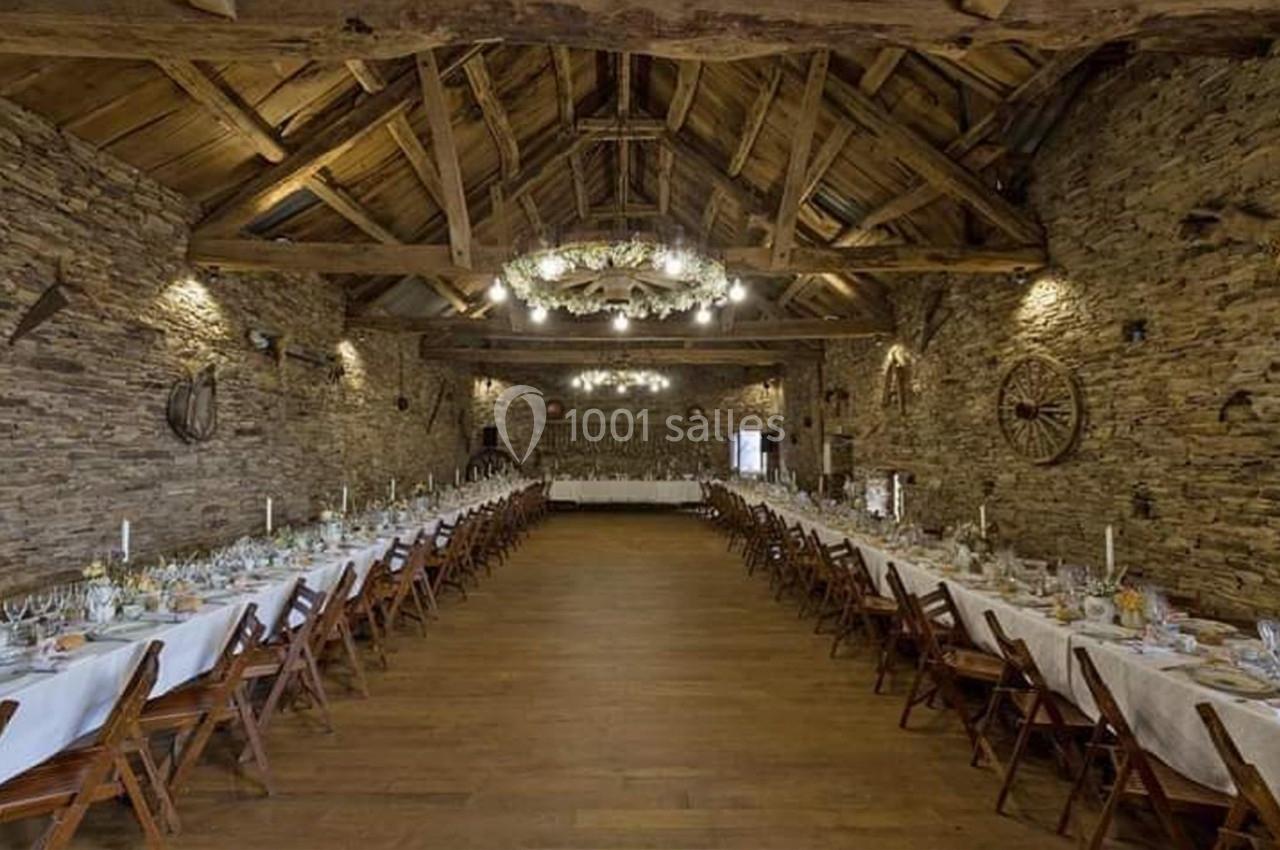 Salle de réception rustique avec murs en pierre, poutres apparentes et tables dressées pour un banquet.