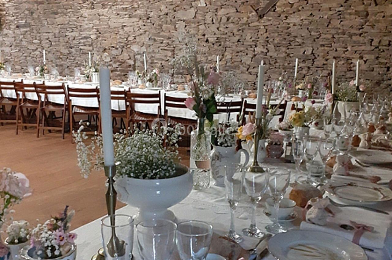 Grande table de réception décorée avec des fleurs, bougies et vaisselle, dans une salle aux murs en pierre apparente.