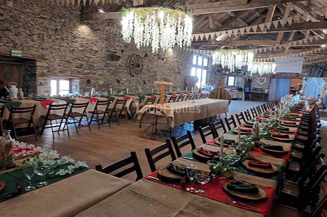 Salle de réception rustique avec tables décorées, nappes en toile de jute, guirlandes suspendues et murs en pierre apparente.