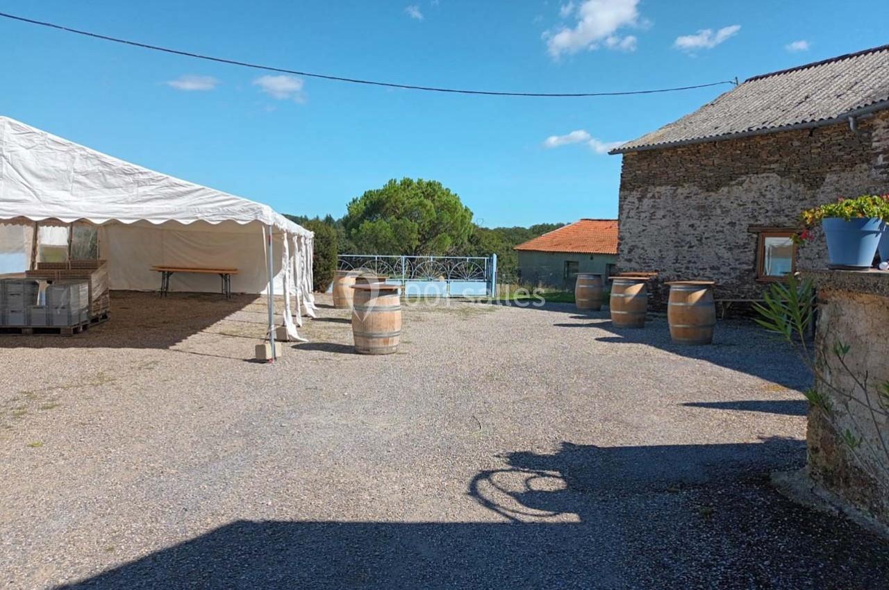 Cour extérieure avec une tente blanche, des tonneaux en bois, un bâtiment en pierre et un ciel dégagé.