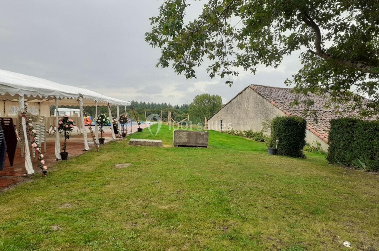 Pelouse avec une tente blanche aménagée pour un événement, entourée de bâtiments en pierre et d'arbres.