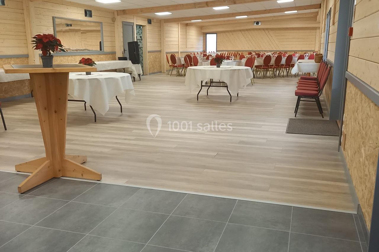 Salle de réception lumineuse avec tables dressées, chaises rouges et décoration sobre dans un espace en bois clair.