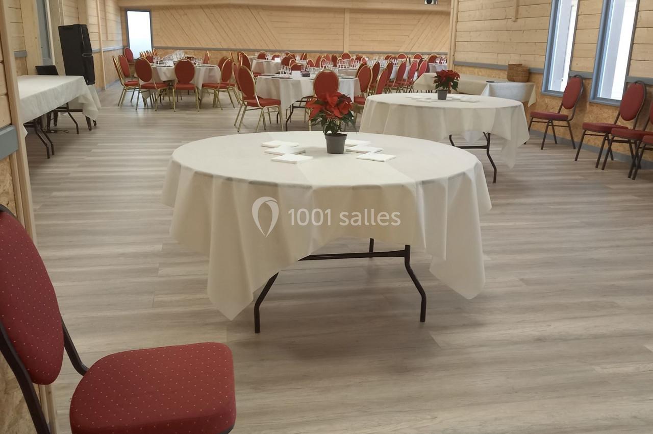 Salle de réception lumineuse avec tables rondes dressées, nappes blanches et chaises rouges.