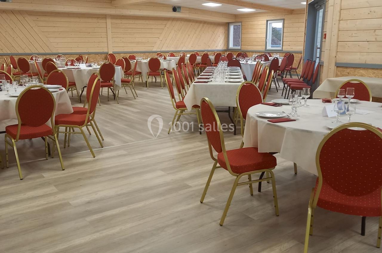 Salle de réception avec tables rondes dressées, chaises rouges et murs en bois clair.