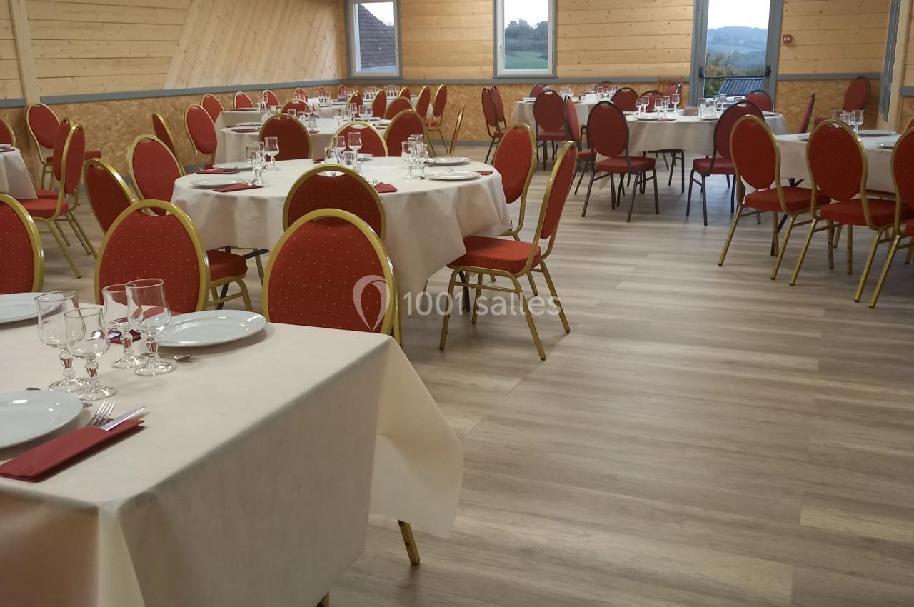 Salle de réception lumineuse avec tables dressées, nappes blanches et chaises rouges, sol en parquet clair.