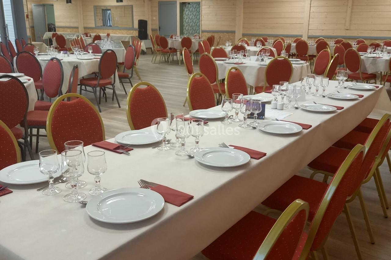 Salle de réception avec des tables dressées, nappes blanches, assiettes, verres et serviettes rouges, prête pour un…