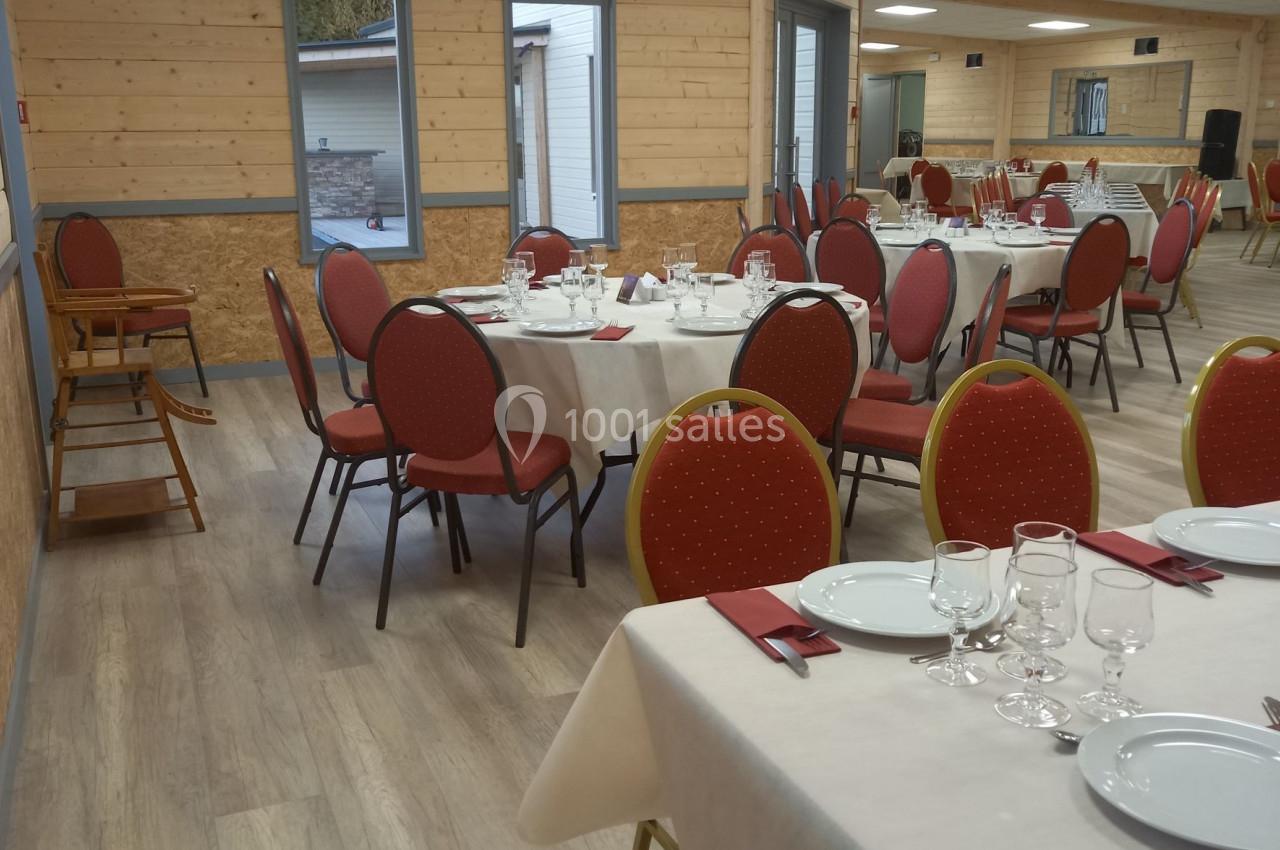 Salle de réception avec tables dressées, nappes blanches, chaises rouges et lumière naturelle provenant des fenêtres.