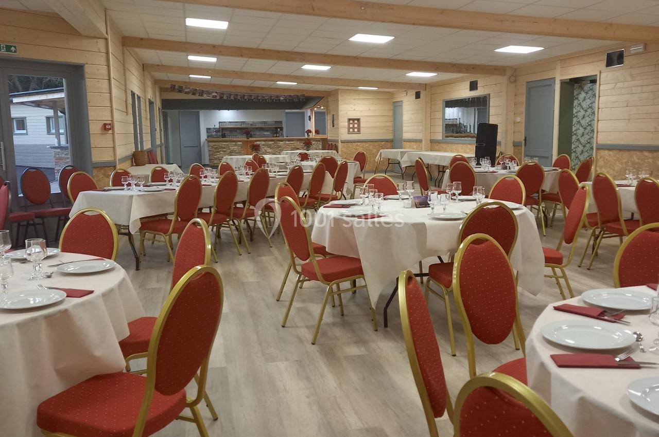 Salle de réception lumineuse avec tables rondes dressées, chaises rouges et décor en bois clair.