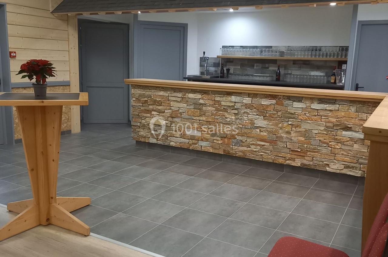 Salle avec comptoir en pierre, tabourets rouges, table haute en bois et éclairage au plafond.