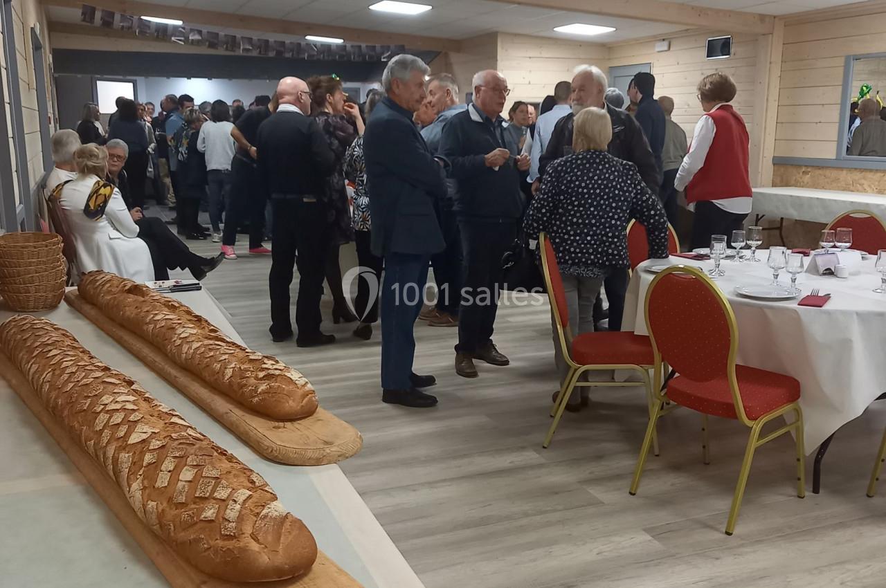 Des convives discutent dans une salle de réception avec des tables dressées et des pains disposés sur une planche au premier…
