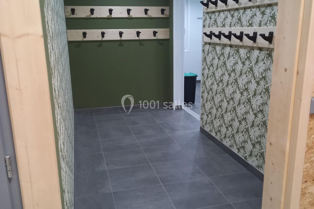 Vestiaire avec murs verts et à motifs végétaux, rangées de patères en bois, sol en carrelage gris.