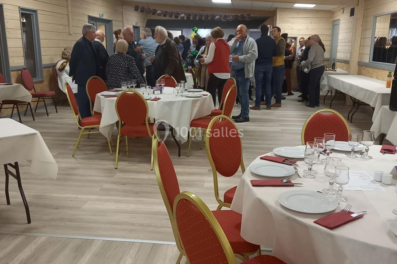 Salle de réception avec des tables dressées et des personnes debout discutant en arrière-plan.