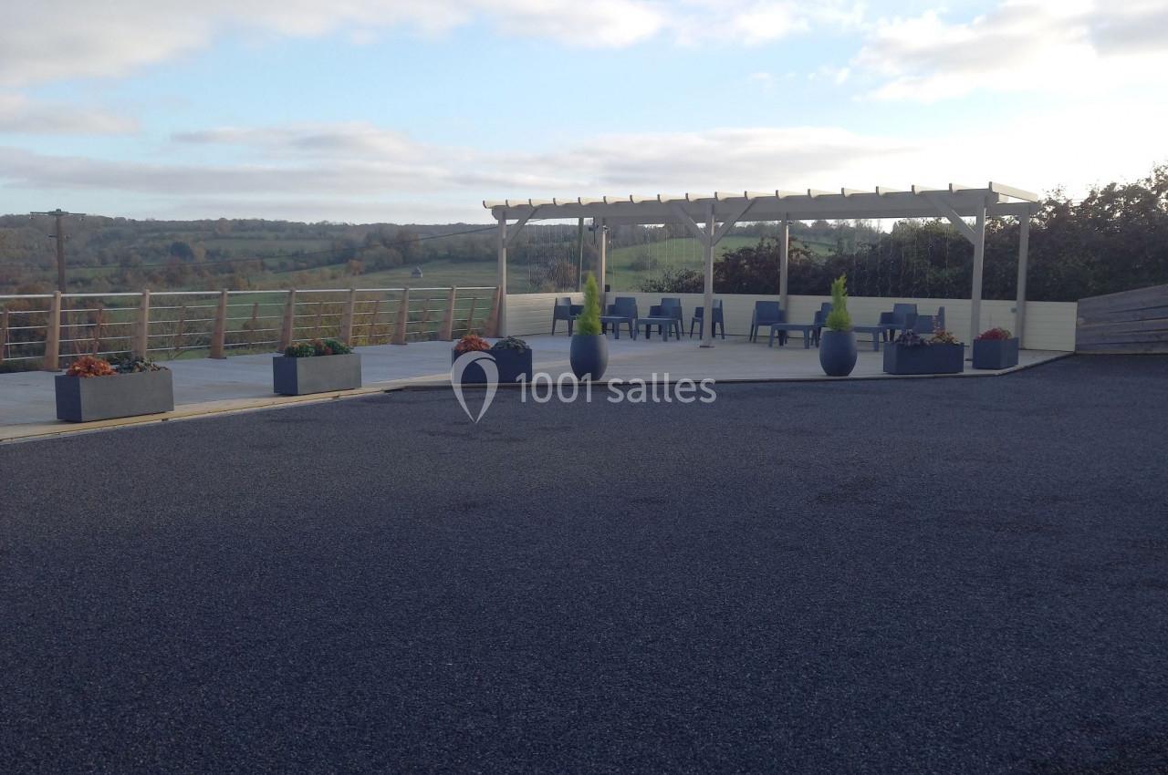 Terrasse extérieure avec pergola, mobilier bleu, pots décoratifs et vue dégagée sur la campagne.