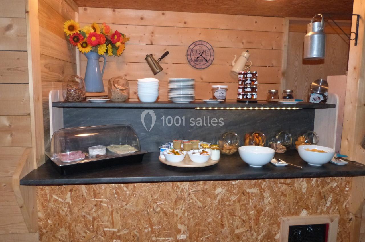 Buffet en bois avec des bols, des pots de yaourt, des céréales, des confitures et une décoration florale.