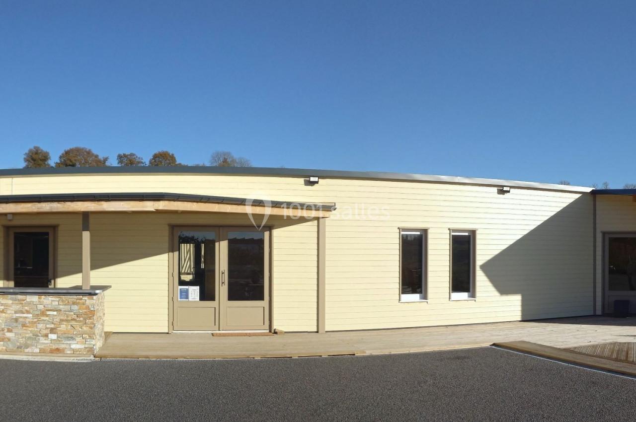 Bâtiment moderne de plain-pied avec façade en bois clair, rampe d'accès et environnement arboré en arrière-plan.
