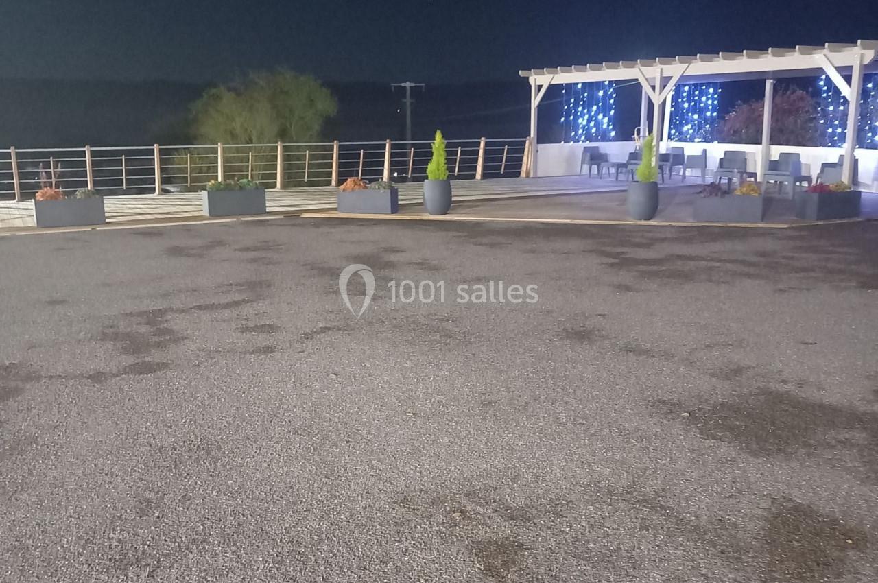 Espace extérieur de nuit avec pergola éclairée, pots de plantes et sol en gravier.