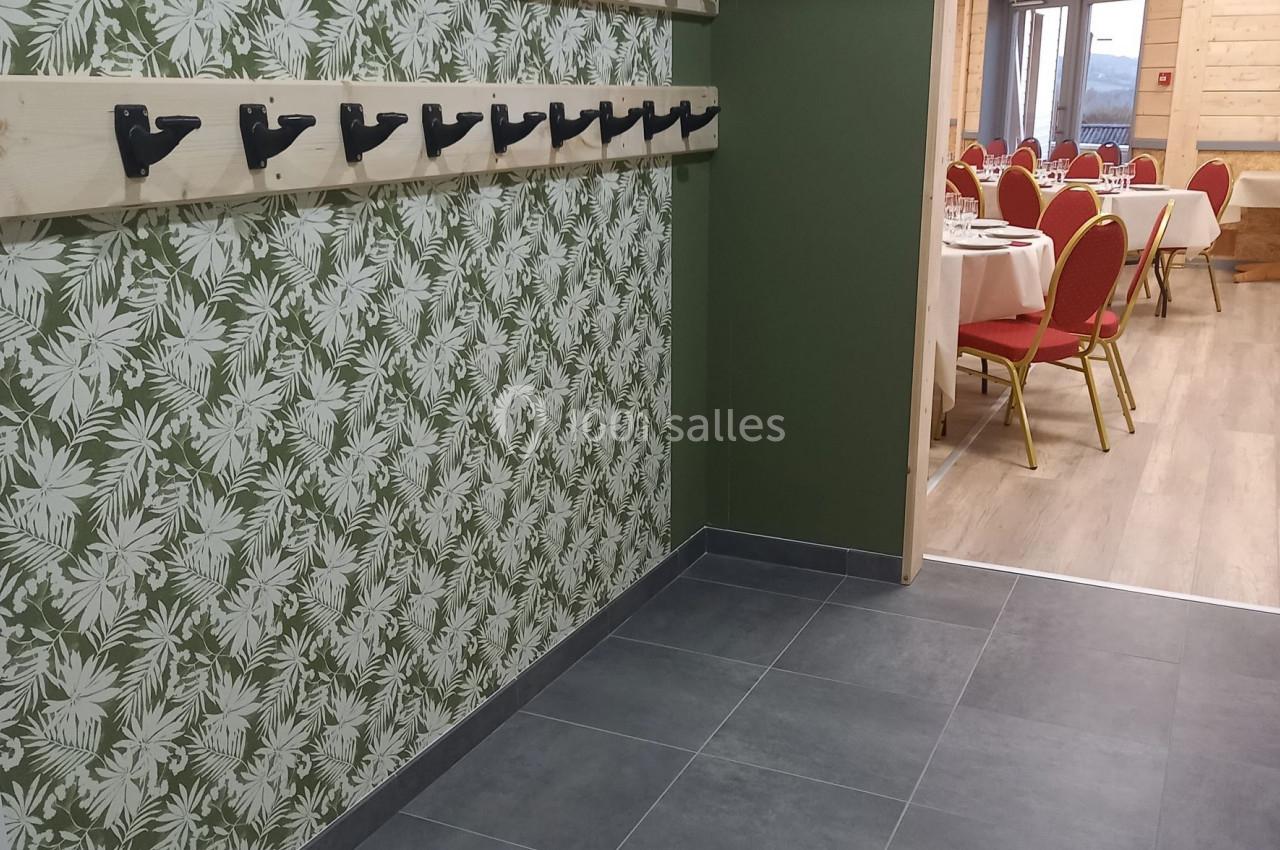 Portemanteaux muraux sur fond de papier peint végétal, avec une salle de réception visible en arrière-plan.