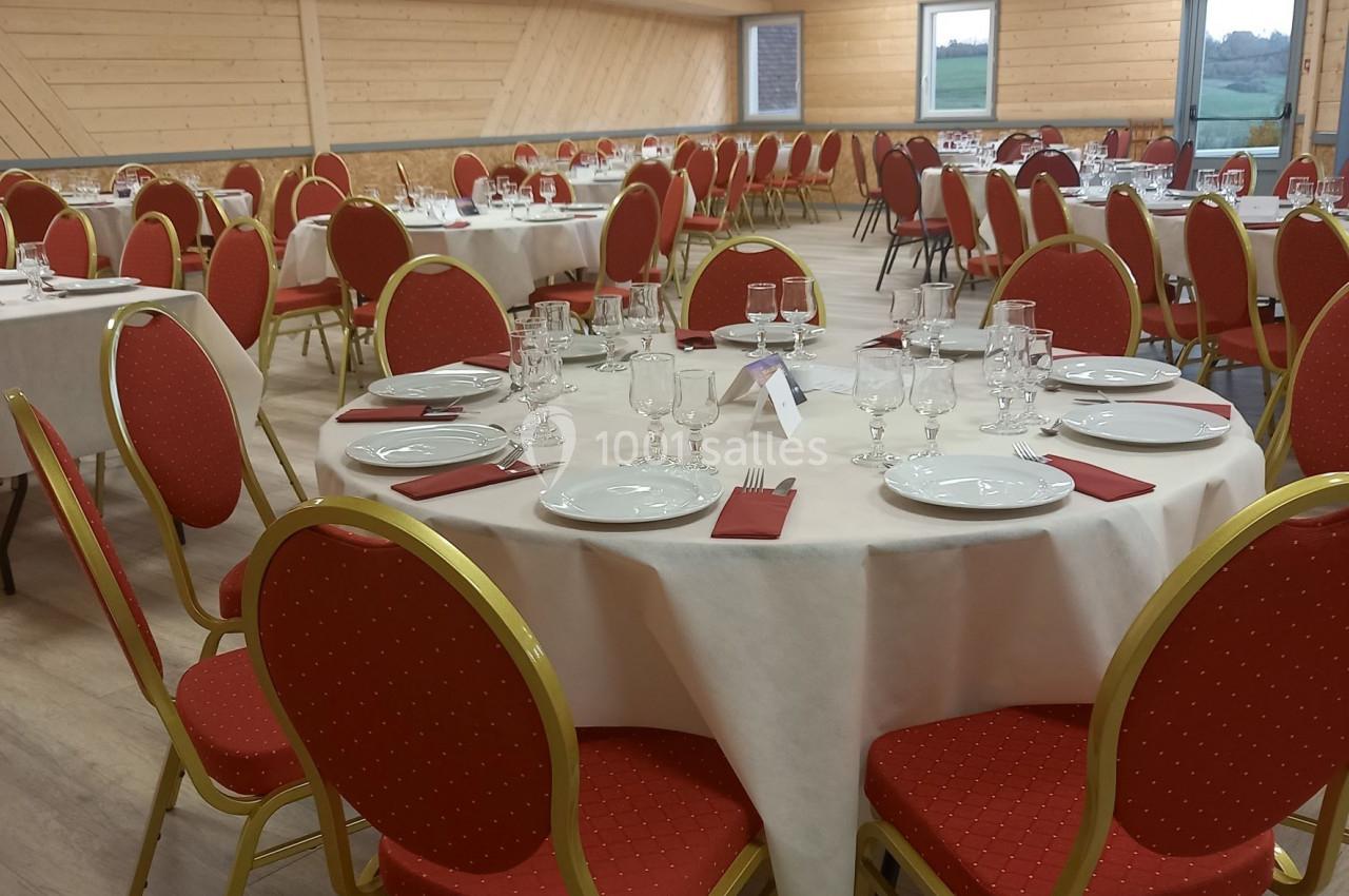 Salle de réception avec tables rondes dressées, nappes blanches, chaises rouges et couverts disposés pour un repas.