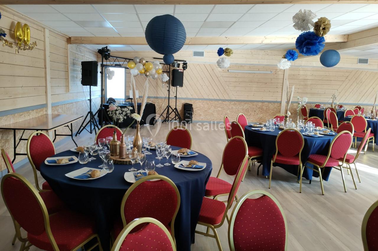Salle décorée pour un événement avec tables rondes, nappes bleues, chaises rouges et suspensions en papier.