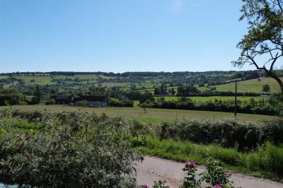 Paysage rural avec une ferme traditionnelle entourée de champs verdoyants et d'arbres sous un ciel nuageux.