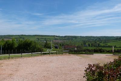 Paysage rural avec une ferme traditionnelle entourée de champs verdoyants et d'arbres sous un ciel nuageux.