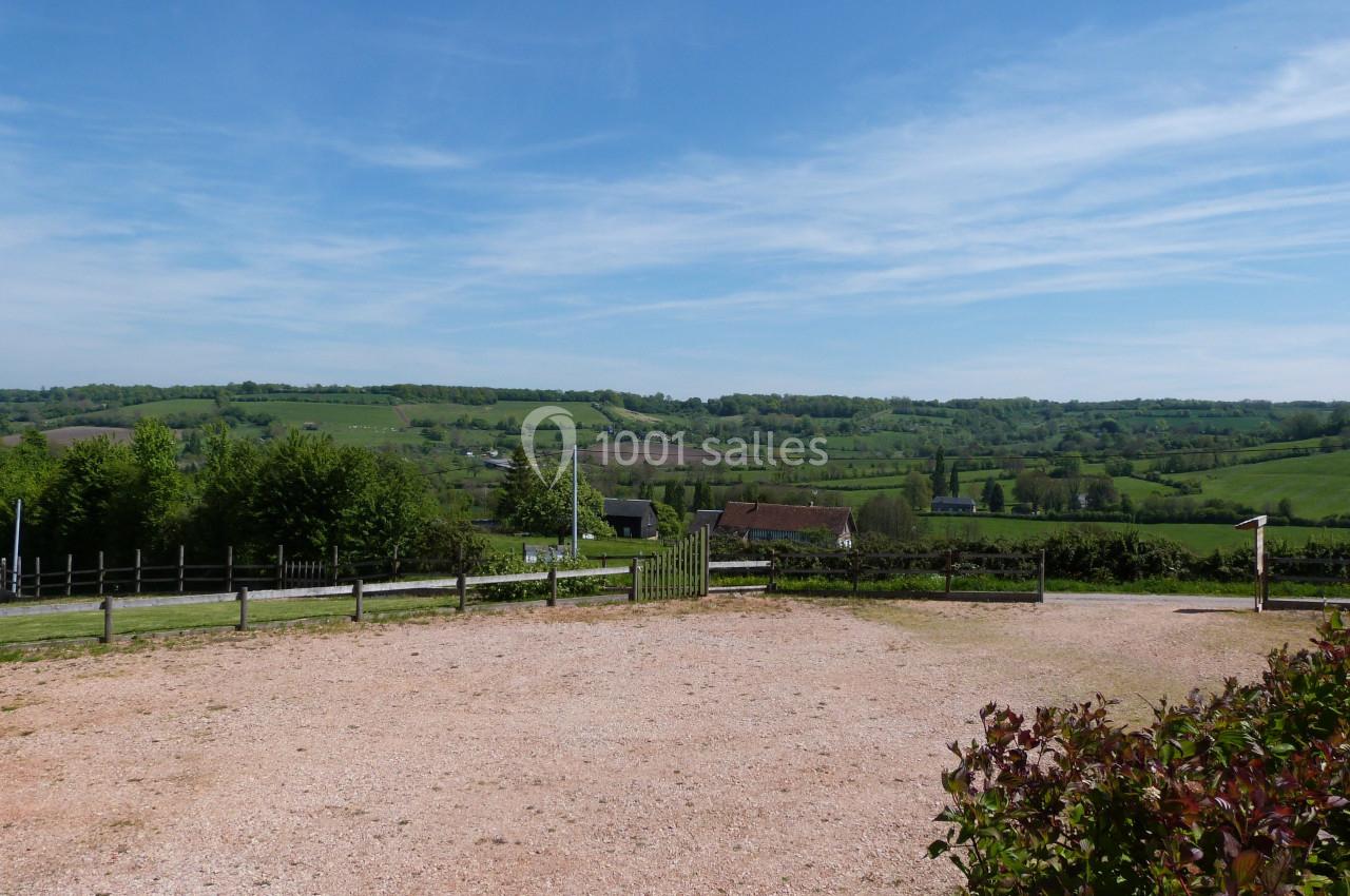 Paysage rural avec collines verdoyantes, quelques maisons dispersées et un ciel bleu parsemé de nuages légers.
