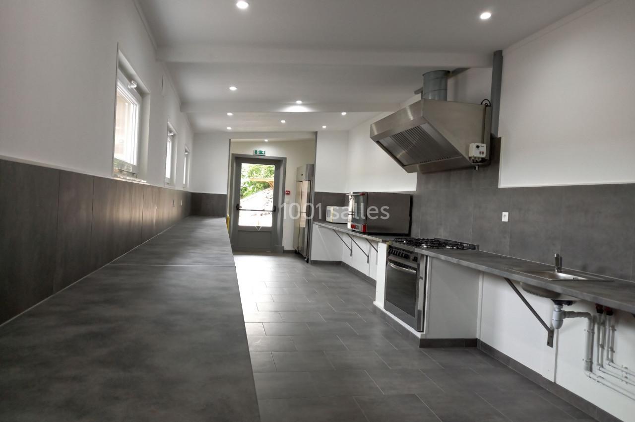 Cuisine professionnelle moderne avec plan de travail long, équipements en inox et éclairage encastré.