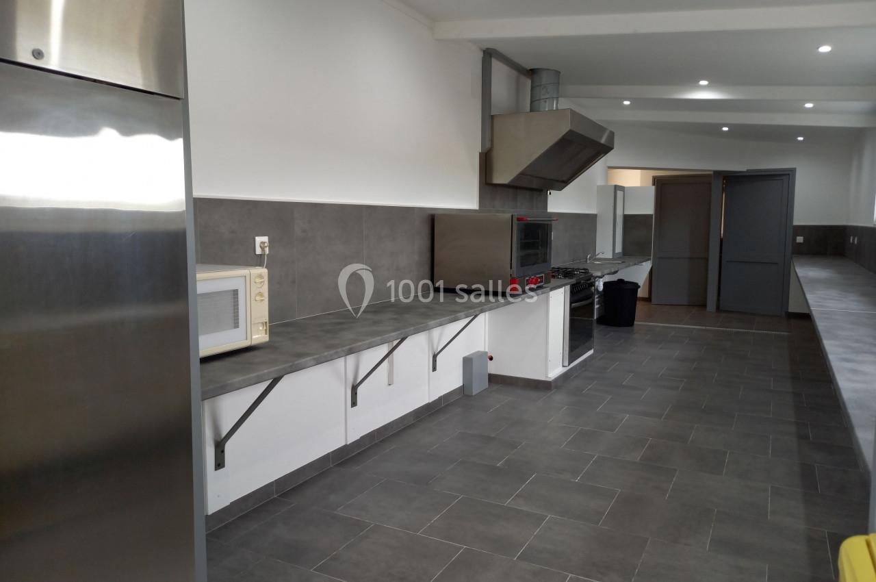 Cuisine professionnelle moderne avec plan de travail en inox, micro-ondes, four et hotte, sol en carrelage gris.