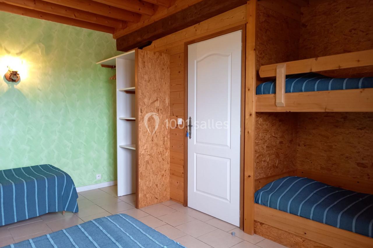 Chambre avec lits superposés en bois, lit simple, murs verts, plafond en bois et sol carrelé.