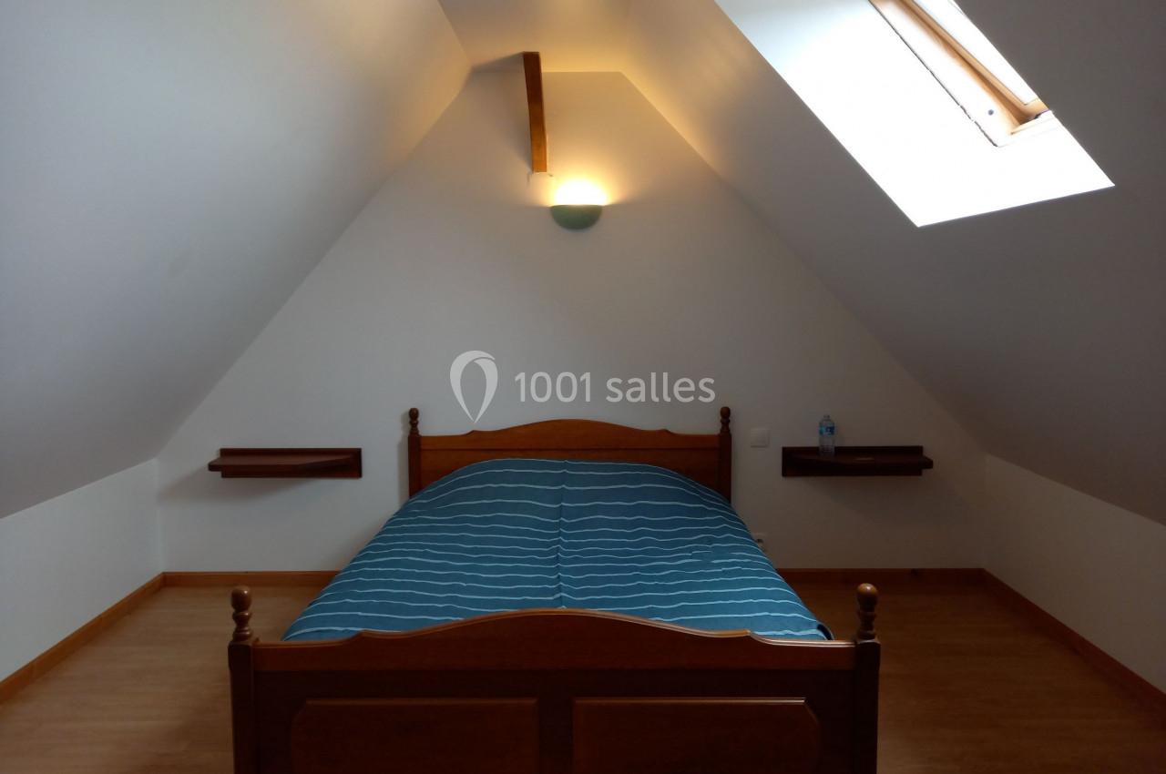 Lit en bois avec une couverture bleue dans une chambre mansardée éclairée par une fenêtre de toit.