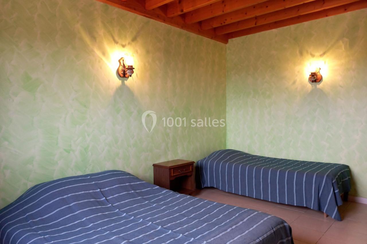 Deux lits simples avec couvre-lits rayés dans une chambre aux murs verts et plafond en bois, éclairée par deux appliques…