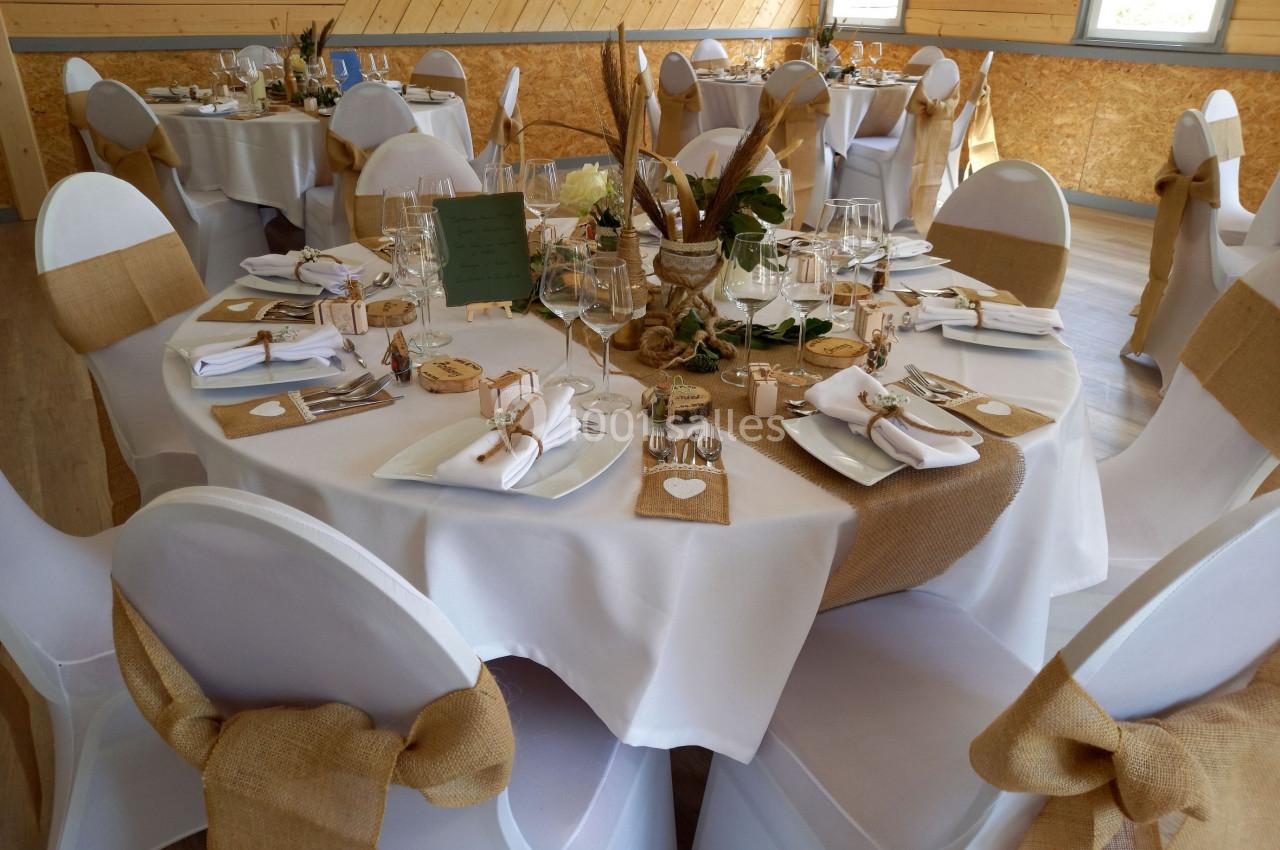 Salle décorée pour un événement avec des tables rondes dressées, nappes blanches et détails en toile de jute.