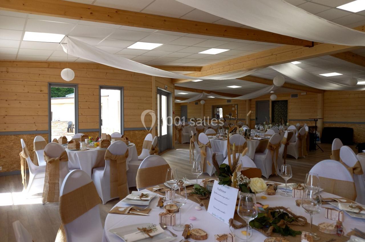 Salle de réception décorée avec des tables rondes, nappes blanches, chaises ornées de nœuds en toile de jute.