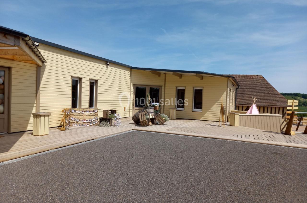 Bâtiment en bois clair avec terrasse en bois, décorations extérieures et ciel dégagé en arrière-plan.