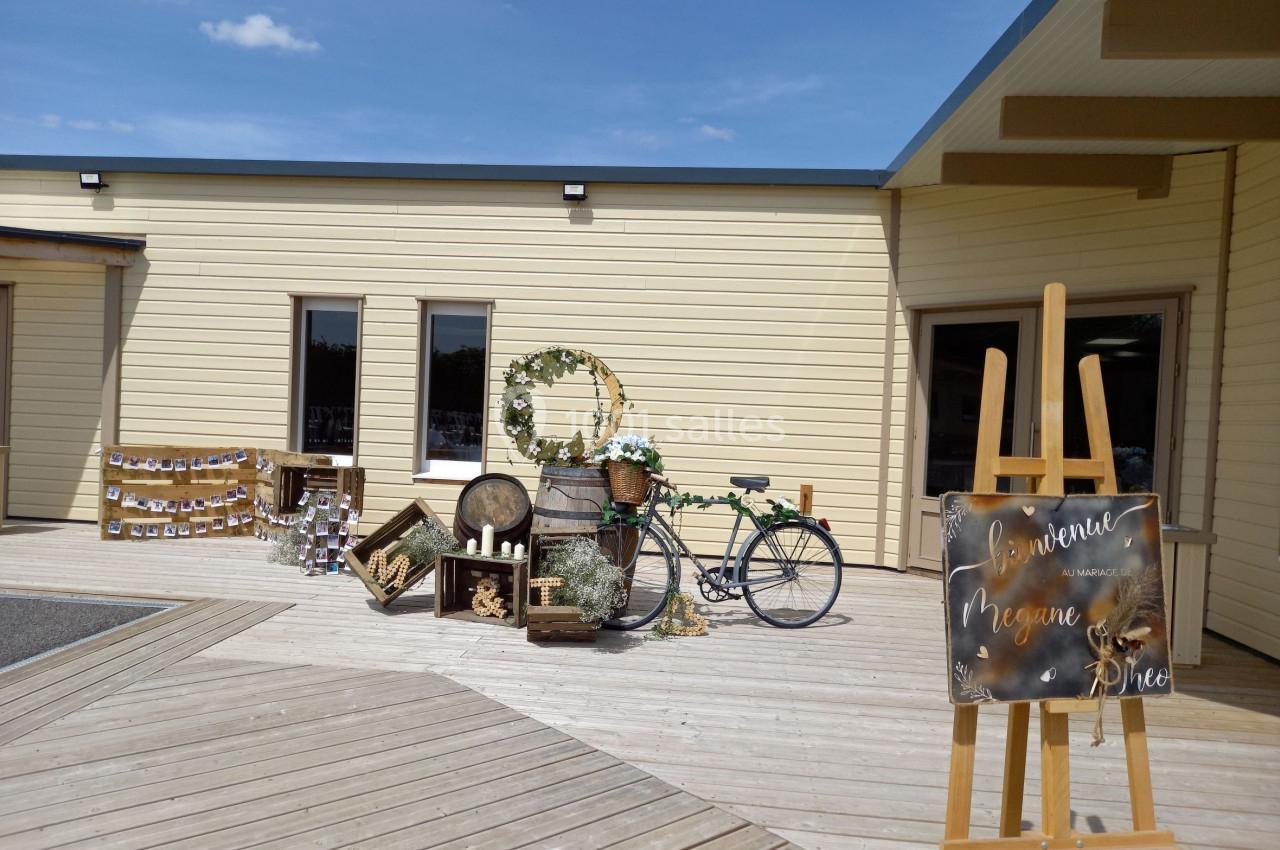 Décoration extérieure avec vélo vintage, caisses en bois, couronne de fleurs et panneau de bienvenue sur chevalet.
