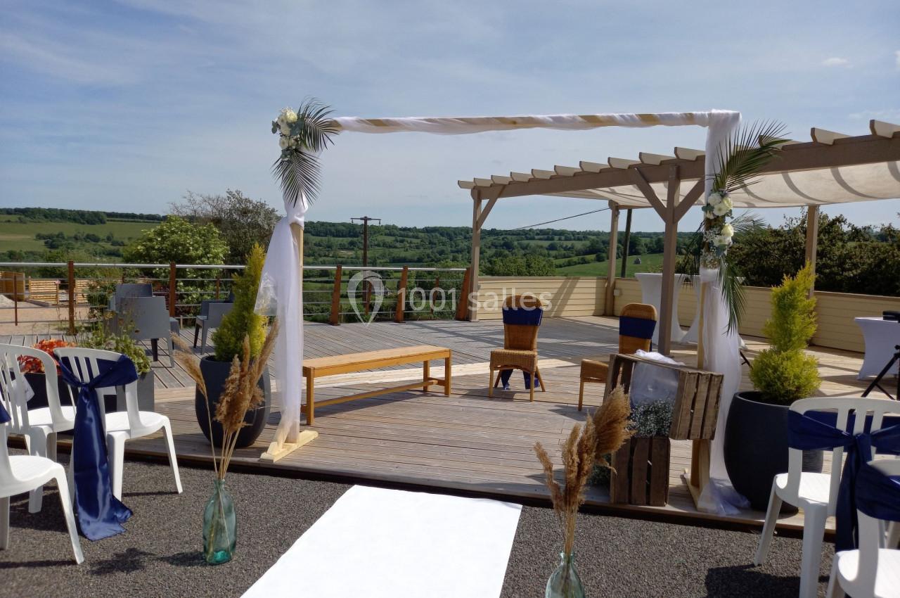 Arche décorée pour une cérémonie en plein air sur une terrasse avec vue sur la campagne environnante.