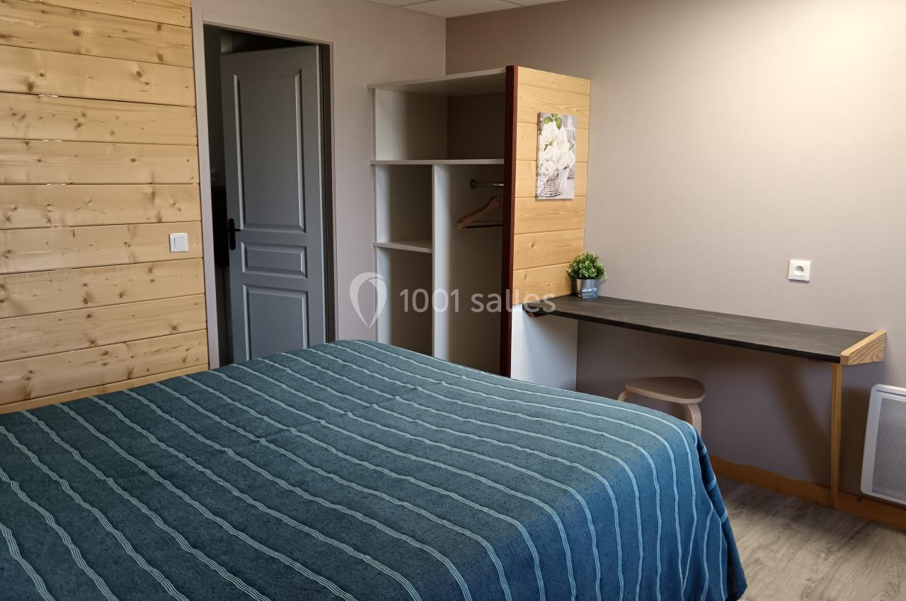 Chambre avec lit double, bureau, étagères ouvertes et mur en bois clair, dans un décor sobre et lumineux.