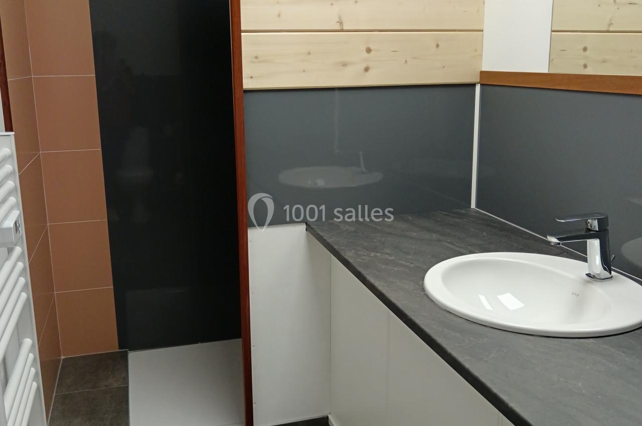 Salle de bain moderne avec lavabo, plan de travail gris, miroir, douche à paroi en bois et carrelage contrasté.