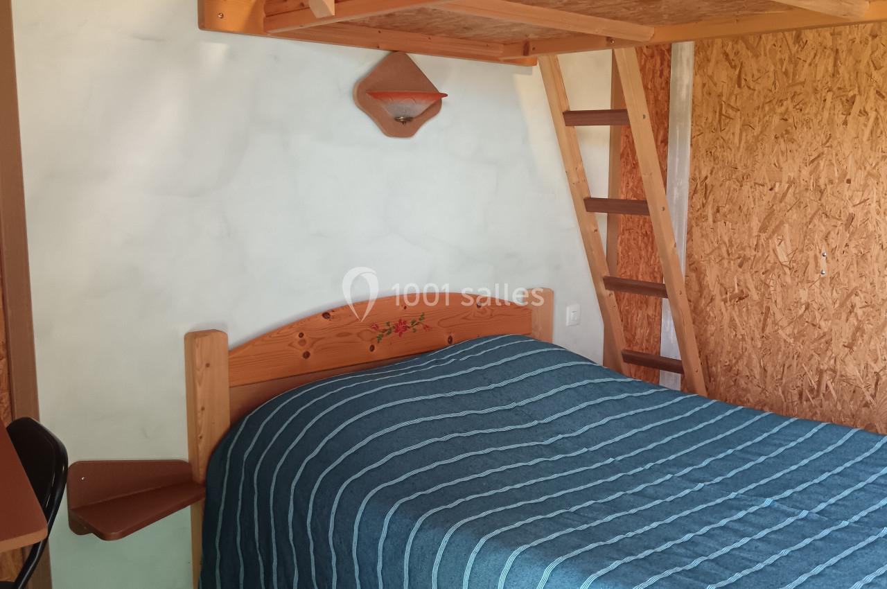 Lit double avec dessus-de-lit bleu, lit superposé en bois au-dessus, échelle et mur en bois dans une chambre simple.