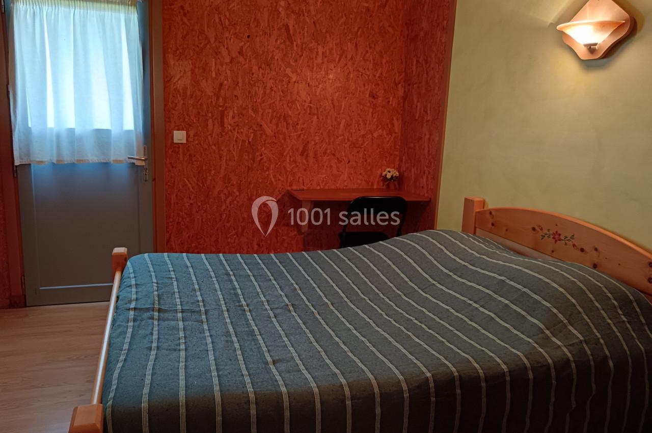 Chambre avec un lit double, une table en bois, une chaise, un mur orange et une porte avec un rideau translucide.