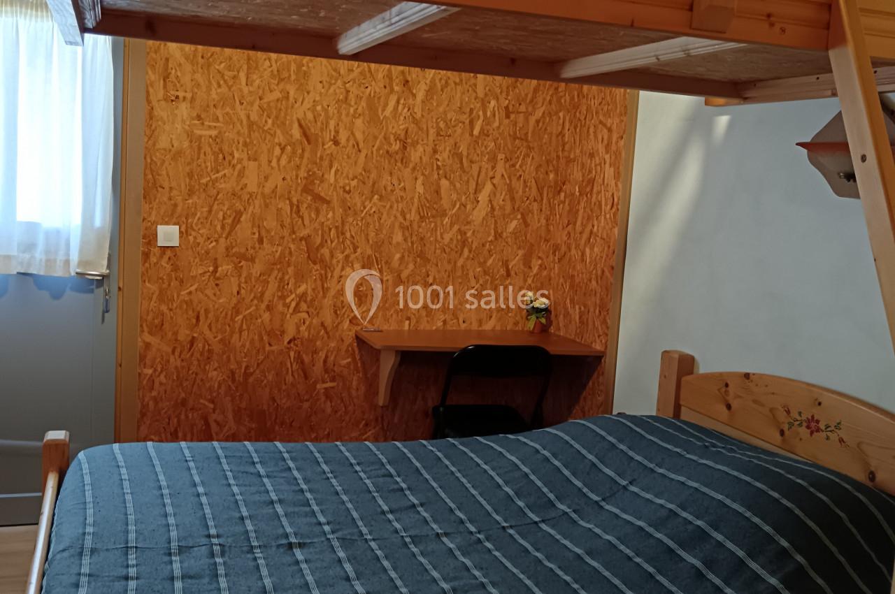 Lit superposé en bois avec une échelle dans une chambre simple, éclairée par une fenêtre avec un bureau en arrière-plan.