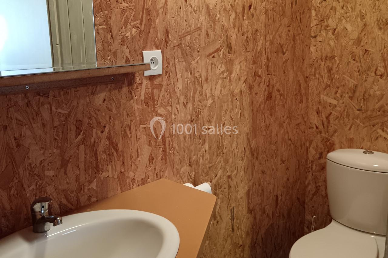 Salle de bain avec murs en panneaux OSB, lavabo avec miroir, toilettes et sol en carrelage vert.