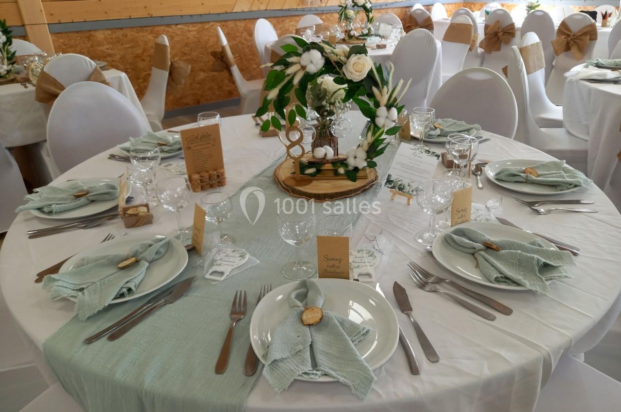 Table décorée pour un mariage avec nappes blanches, serviettes vertes, centres de table floraux et menus en papier kraft.