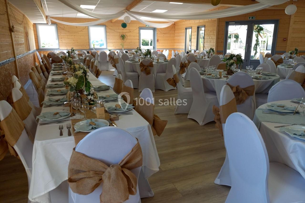 Salle de réception décorée pour un événement, avec tables dressées, nappes blanches et chaises ornées de nœuds en toile de…