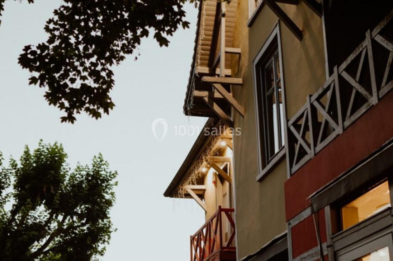 Façade d'une maison colorée avec balcons en bois, entourée de végétation sous un ciel clair en soirée.