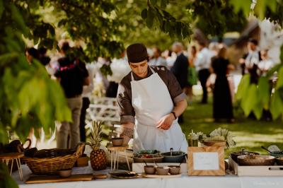 Un chef cuisine sur un barbecue rond dans un jardin aménagé avec des tables et des plantes.