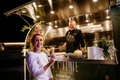 Un chef cuisine sur un barbecue rond dans un jardin aménagé avec des tables et des plantes.