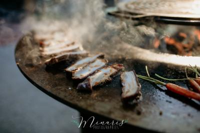 Un chef cuisine sur un barbecue rond dans un jardin aménagé avec des tables et des plantes.