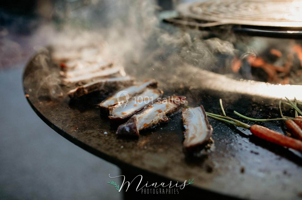 Tranches de viande grillées sur une plancha avec des légumes, entourées de vapeur.