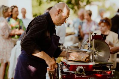 Un chef cuisine sur un barbecue rond dans un jardin aménagé avec des tables et des plantes.